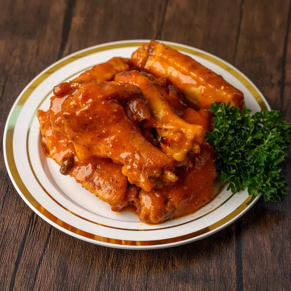 A white plate with gold trim holds several buffalo chicken wings and a sprig of parsley.