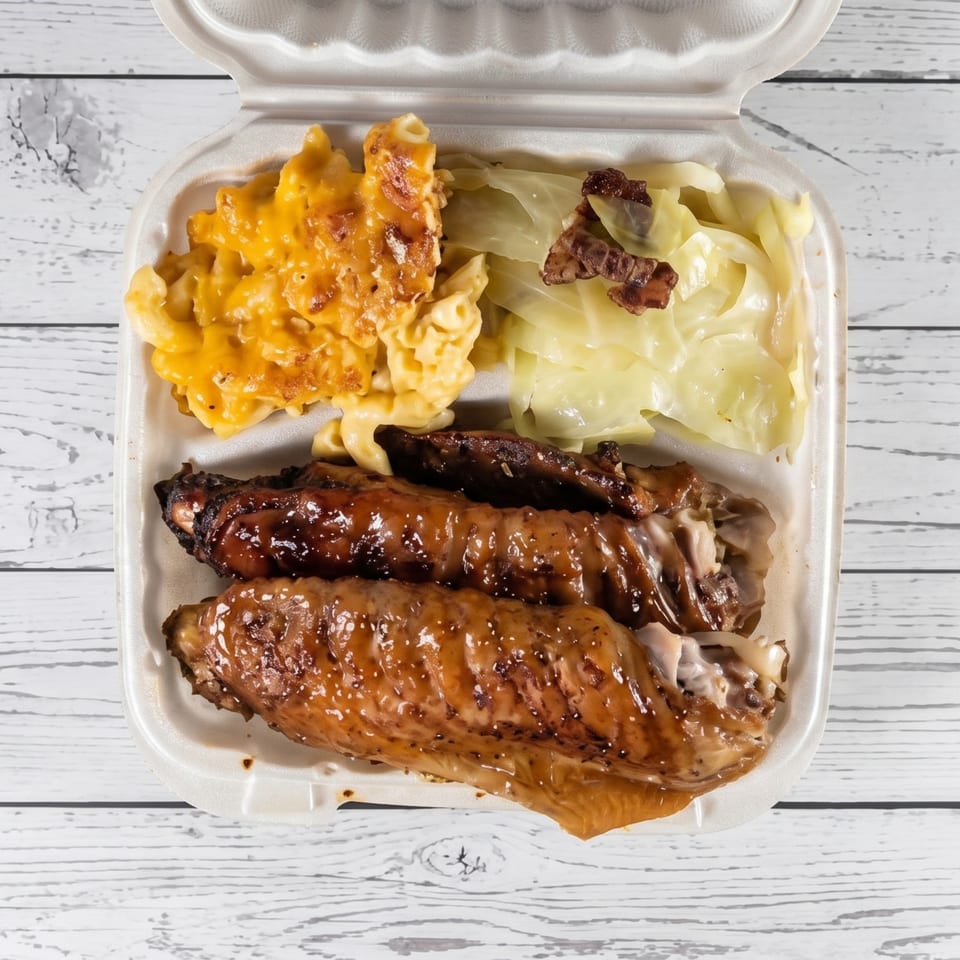 Takeout container with glazed turkey wings, macaroni and cheese, and cooked cabbage.