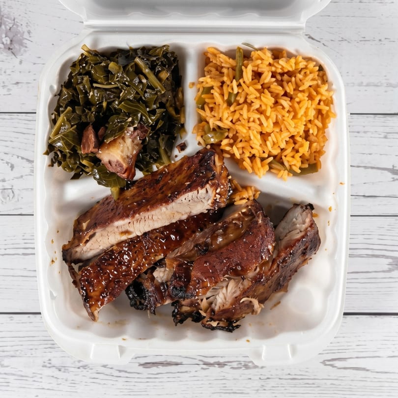 Barbecue ribs with collard greens and seasoned rice in a white takeout container.