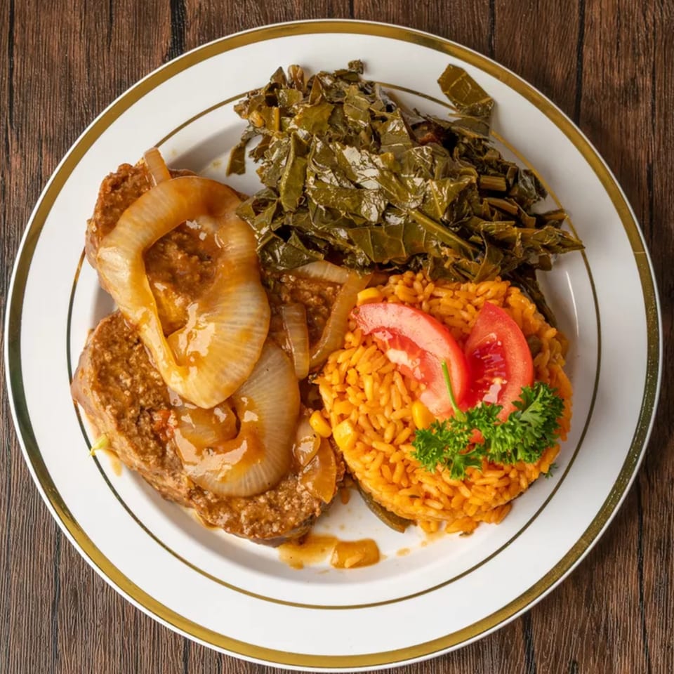 A plate of meatloaf with onions, collard greens, and yellow rice with tomatoes and parsley.