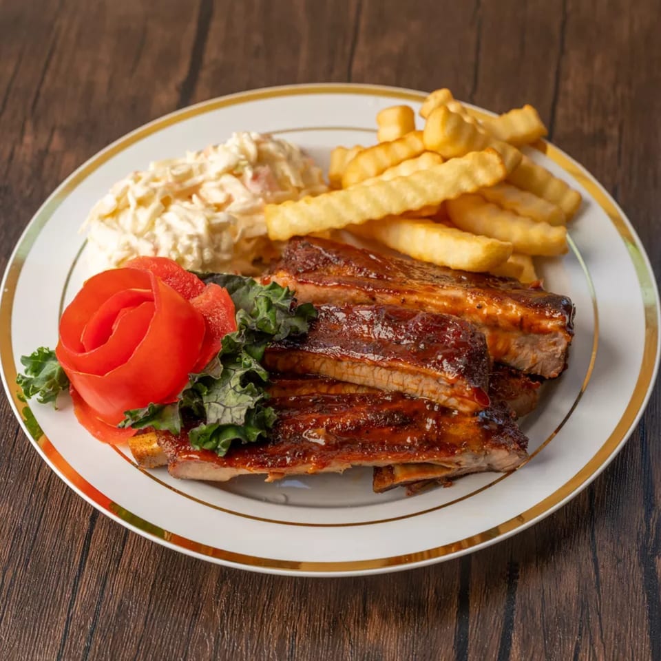 Ribs with barbecue sauce, crinkle-cut fries, coleslaw, and a tomato rose on a white plate.