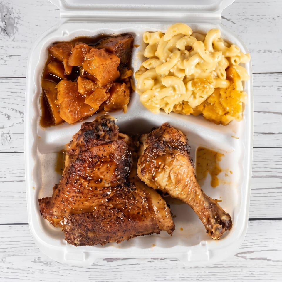 Grilled chicken, macaroni and cheese, and candied yams in a white takeout container.